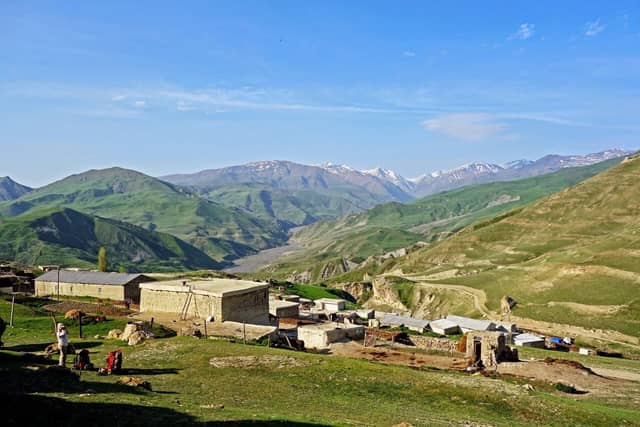 Buduq kəndinin daş evləri və arxada uzanan dağ vadisi ilə qarlı zirvələr.