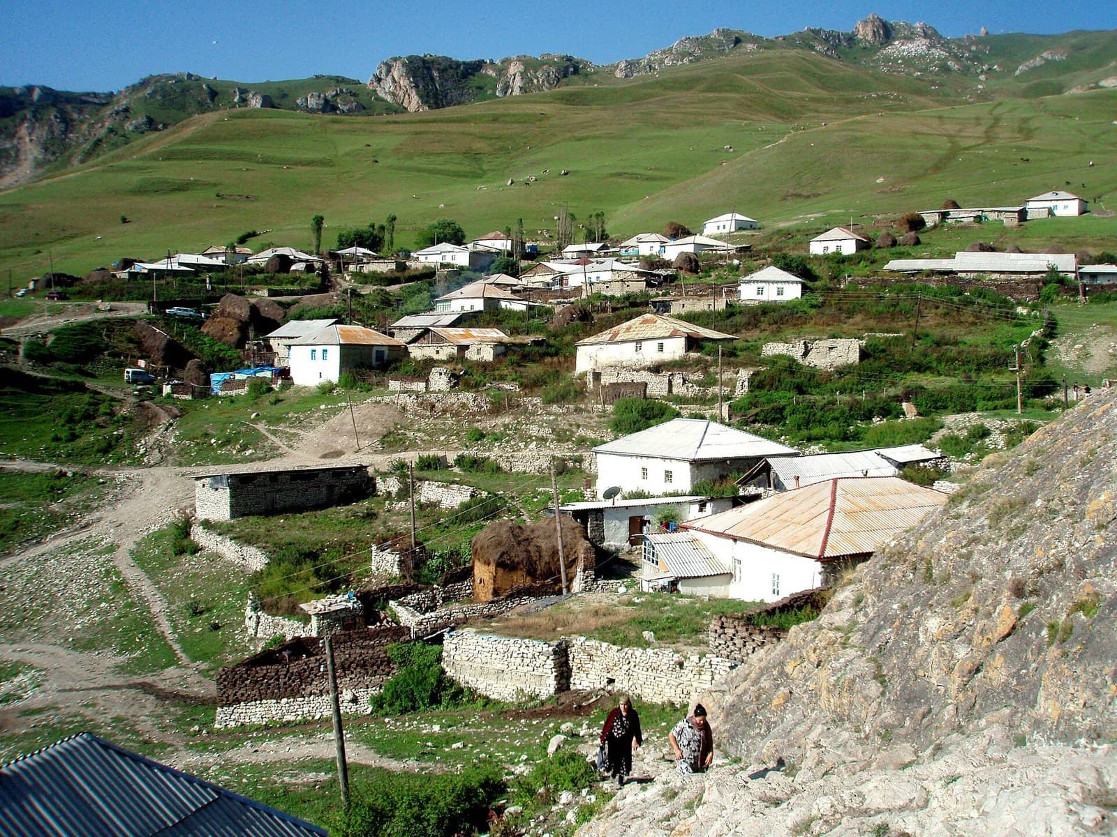 Yaşıl dağ yamacında yerləşən Cek kəndinin evləri və arxadakı qayalı təpələr.