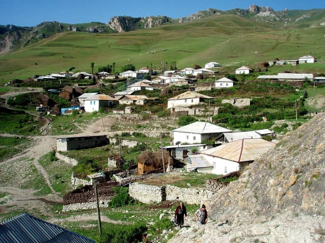 Yaşıl dağ yamacında yerləşən Cek kəndinin evləri və arxadakı qayalı təpələr.