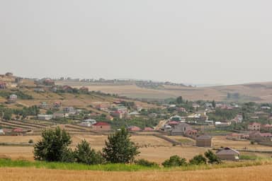 Дома с красными крышами в селе Чухурюрд, перед ними — жёлтое пшеничное поле, Шемахинский район