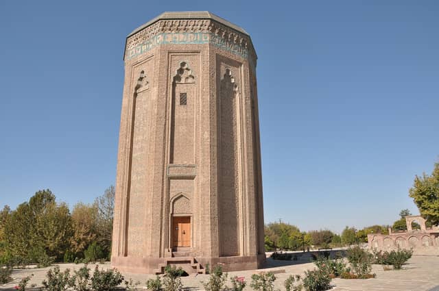 Möminə Xatun türbəsi, Naxçıvan: kufi yazılı firuzəyi qurşaqlı, naxışlı kərpicdən onbucaqlı hündür türbə və önündə qızılgül kolları