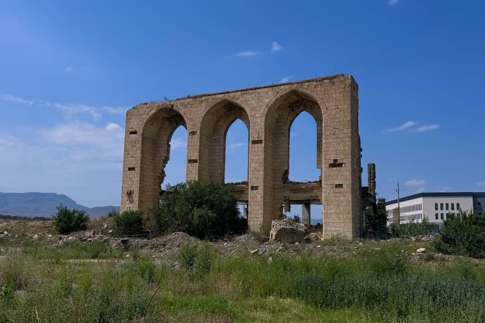 Ağdamda dağıdılmış Dövlət Dram Teatrının üç tağlı daş fasadı, 2024-cü ilin avqustu, arxada dağlar