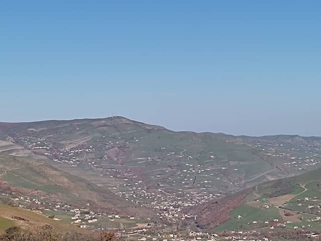 Yardımlı rayonunda dağ yamacları boyunca səpələnmiş kənd evləri və mavi səma altında zirvə.