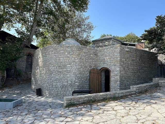 Basqalda bərpa olunmuş daş hamam binası və taxta giriş qapısı.