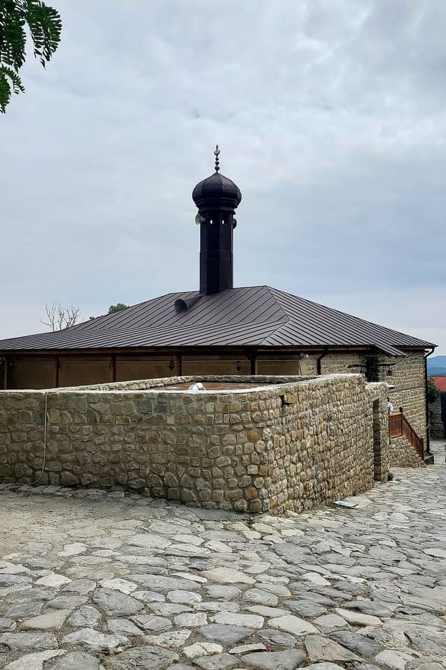 Basqalda daş hasarın arxasında qara minarəli Hacı Bədəl məscidi.