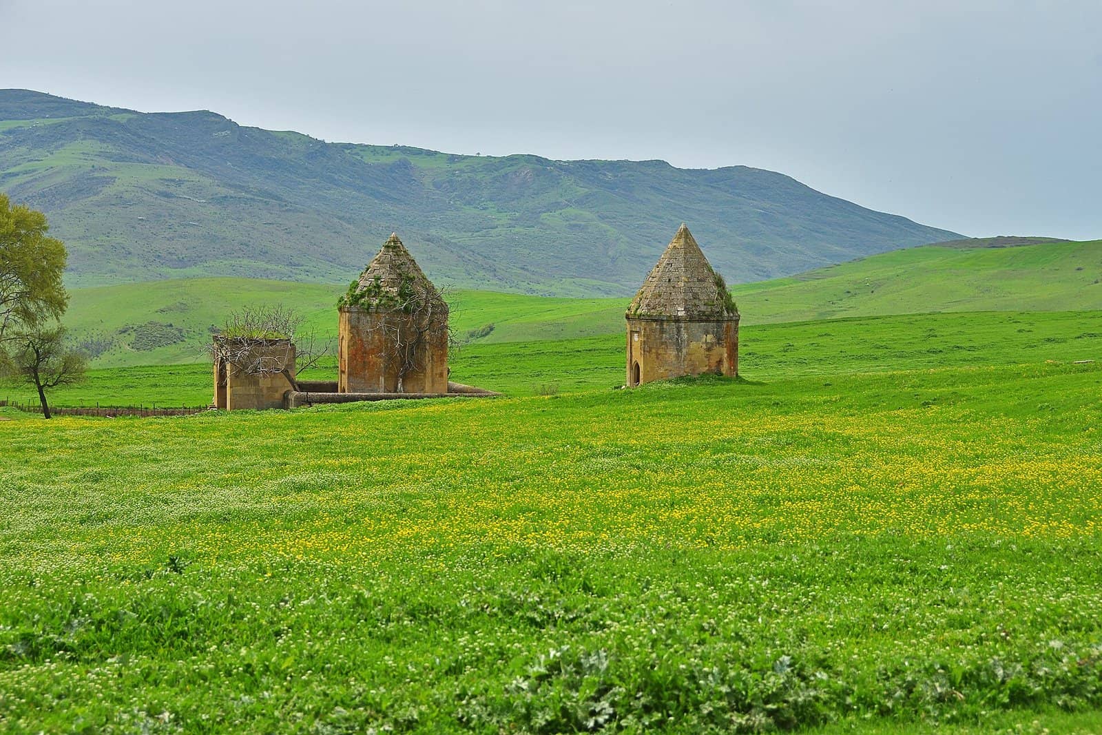 Yaşıl çəmənlikdə üç daş Kələxana türbəsi və arxada dağ silsiləsi.