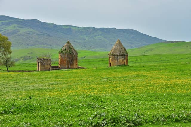 Yaşıl çəmənlikdə üç daş Kələxana türbəsi və arxada dağ silsiləsi.