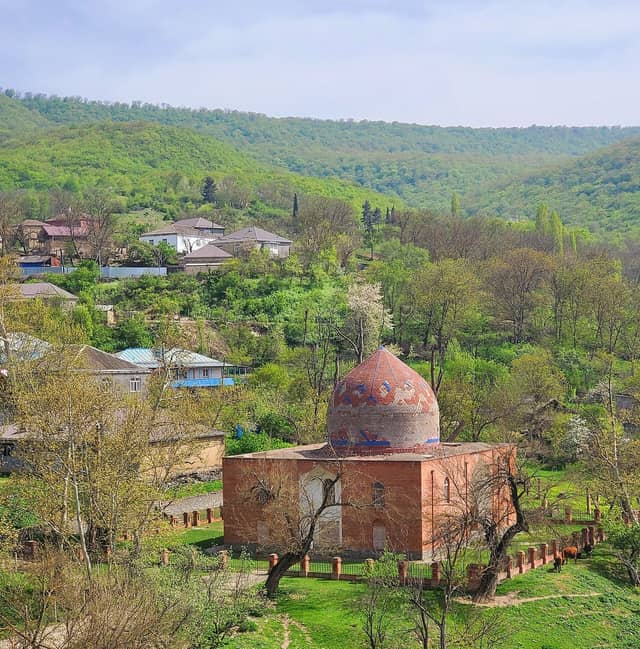 Həzrə kəndində meşəli təpələrin qarşısında naxışlı günbəzli Şeyx Cüneyd türbəsi.