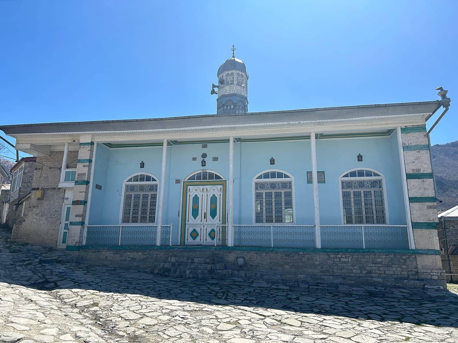 Lahıcda mavi fasadlı Zəvəro məscidi və önündə daş döşənmiş küçə.